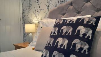 A bedroom with a tufted headboard, a patterned pillow, a bedside lamp, and a wall with a floral wallpaper.