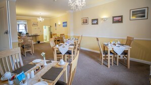 A dining area with wooden tables and chairs, a chandelier, and wall-mounted light fixtures. - The Briarfields (Torquay)