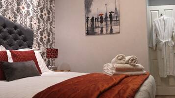 Una habitación de hotel con una cama, un cuadro de personas bajo la lluvia y una lámpara, además de un perchero para abrigos.