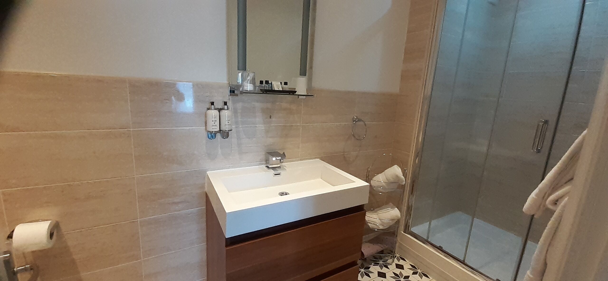 A modern bathroom with a white sink, mirror, and tiled walls. There is a glass shower enclosure and a towel rack.