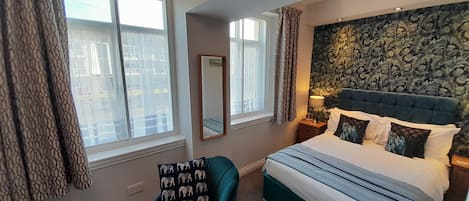 Une chambre à coucher avec un grand lit, une chaise, un miroir et une fenêtre avec des rideaux.