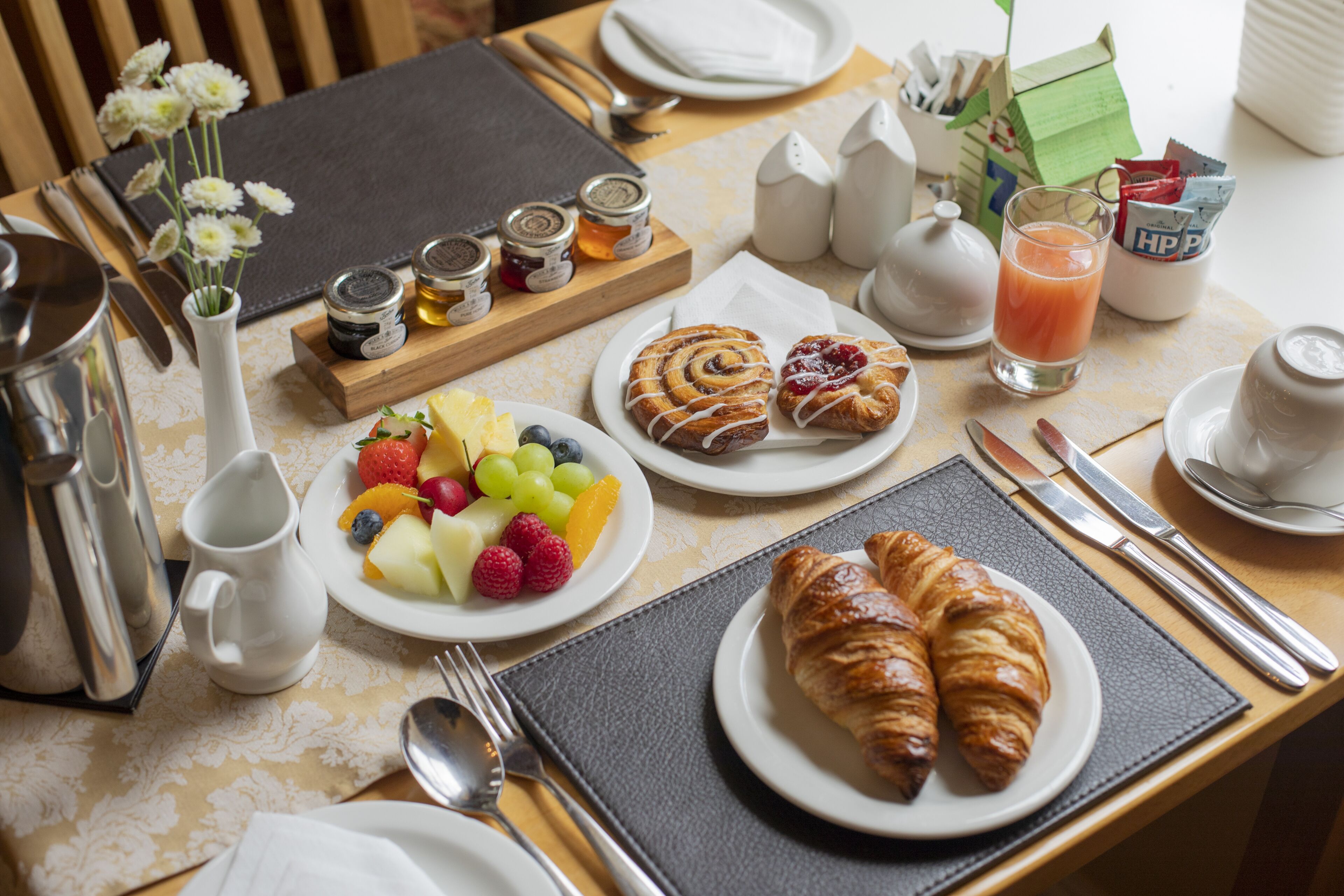 Une table de petit-déjeuner avec des croissants, des fruits et un verre de jus.