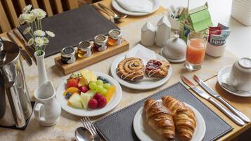 Une table de petit-déjeuner avec des croissants, des fruits et un verre de jus.