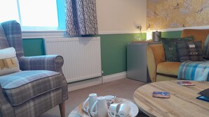 A cozy living room with a plaid armchair, a sofa with a plaid blanket, a wooden coffee table with a tray of white cups and saucers, and a radiator. - The Briarfields (Torquay)