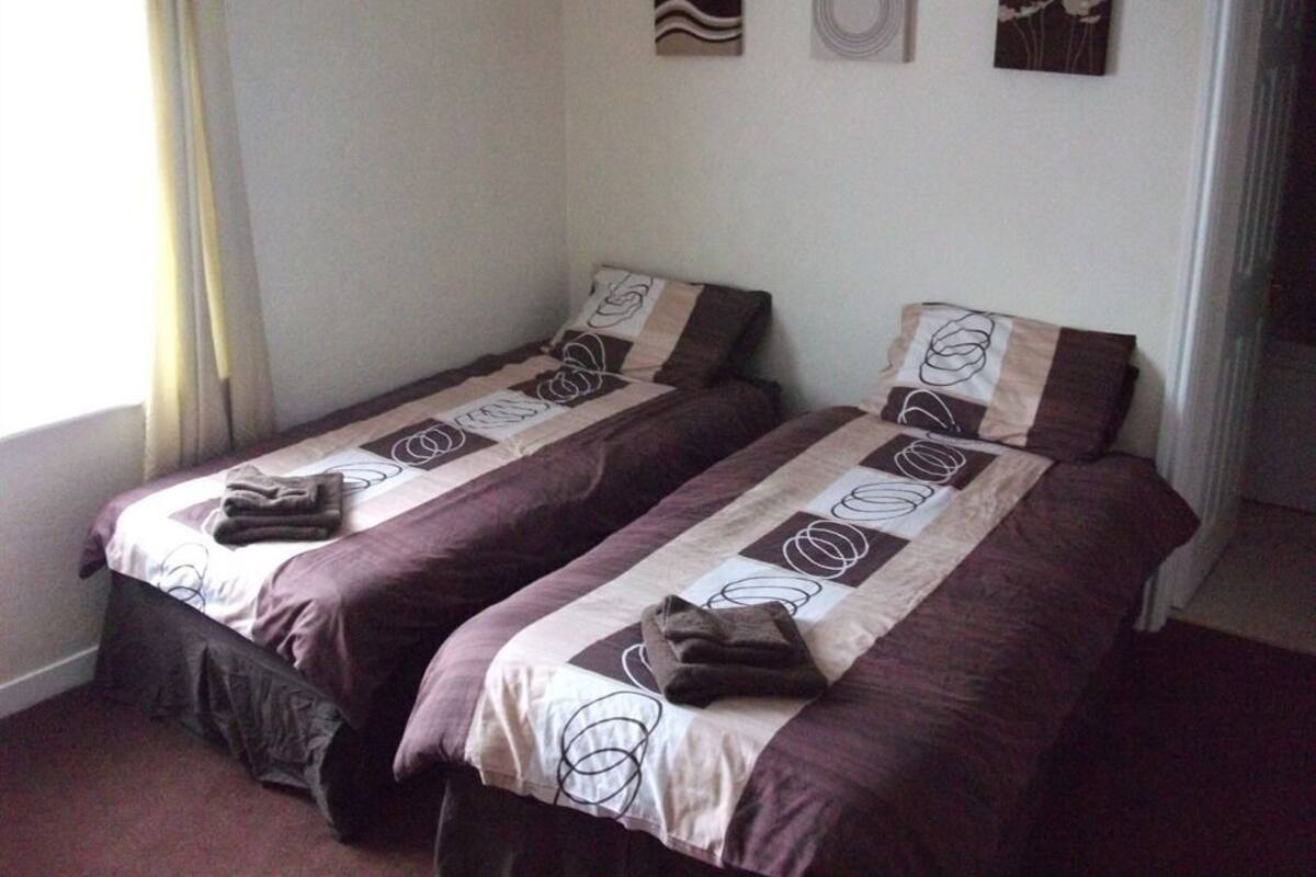 Two single beds with patterned bedding, a window with curtains, and three wall art pieces.