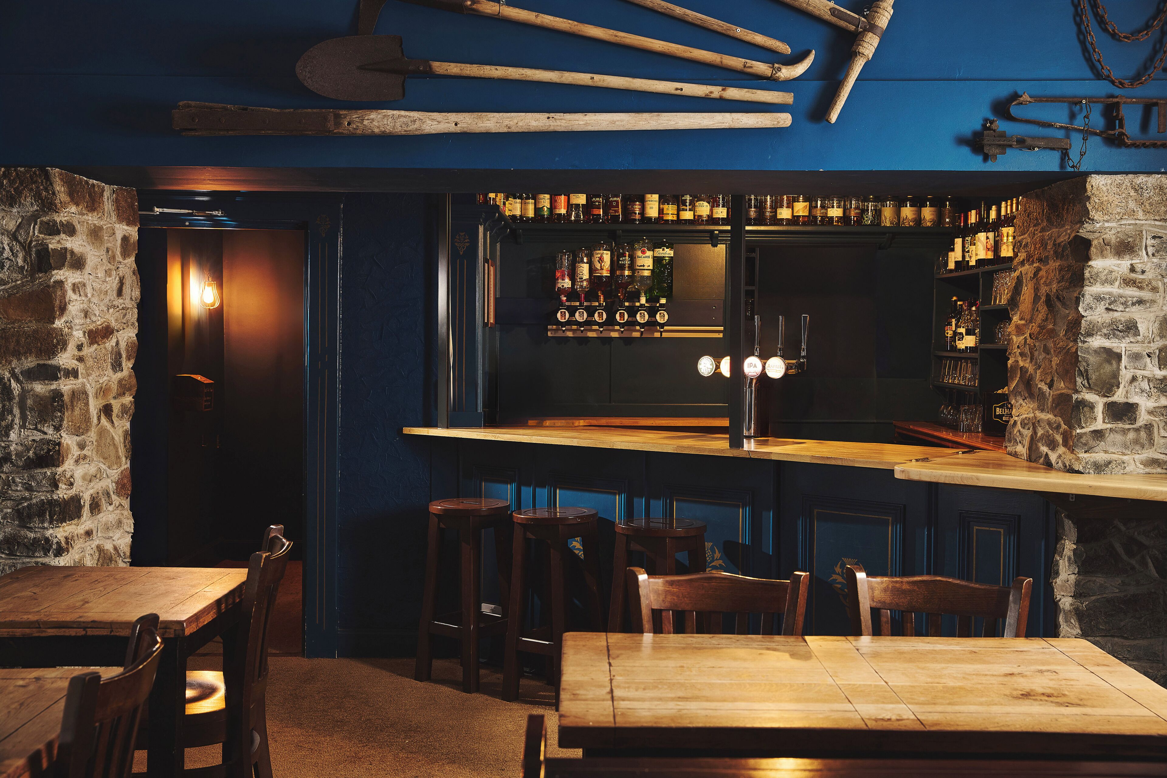 A bar area with wooden stools, a bar counter, and a selection of bottles.