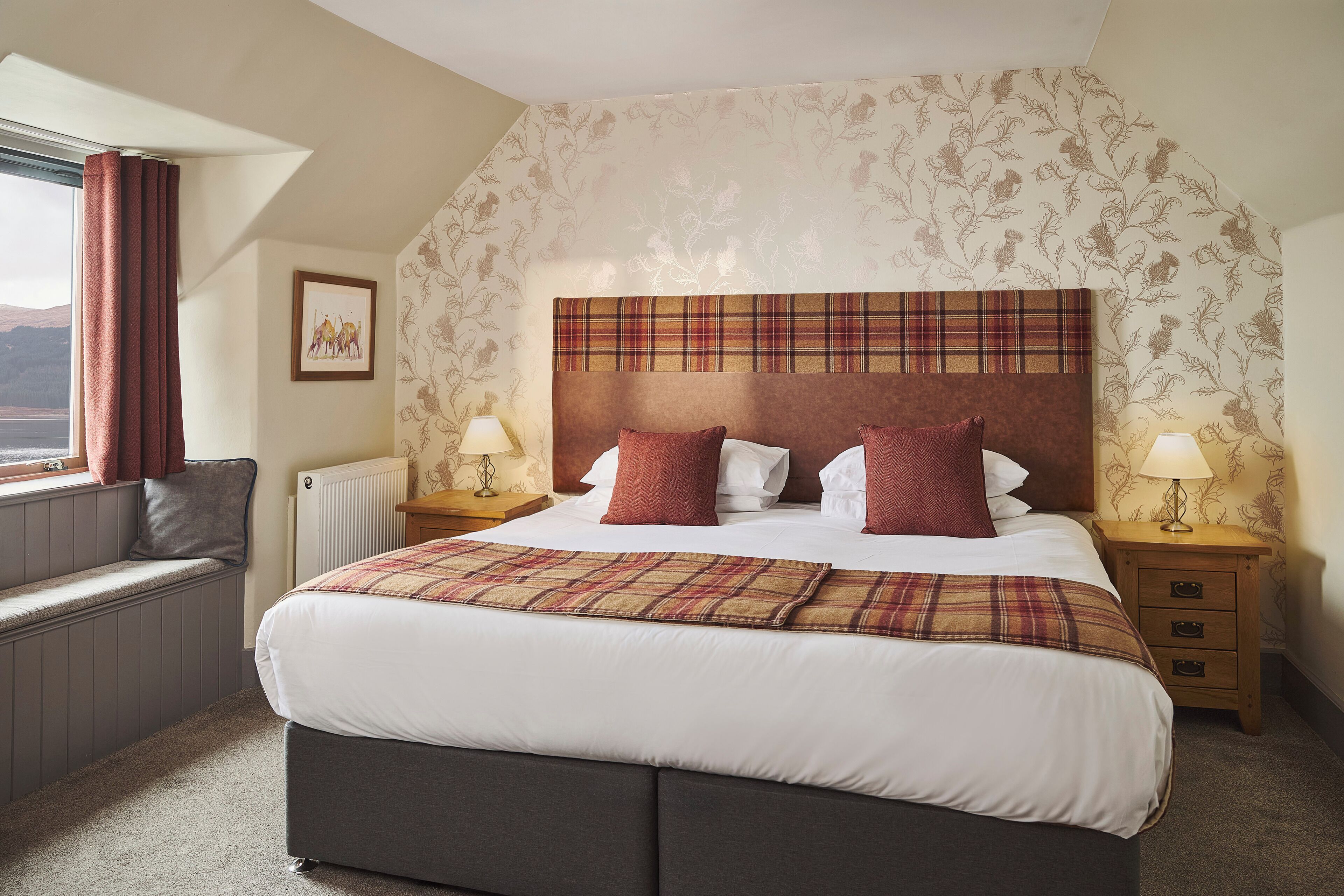 Habitación de hotel con una cama grande, dos mesitas de noche, una ventana con cortinas, un radiador y una pared con estampado floral.
