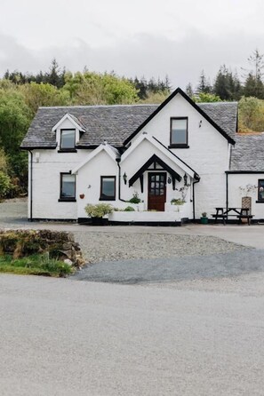 A white two-story house with a pitched roof, a front porch, and a small garden area. - Inn at Port nan Gael (Isle of Mull)