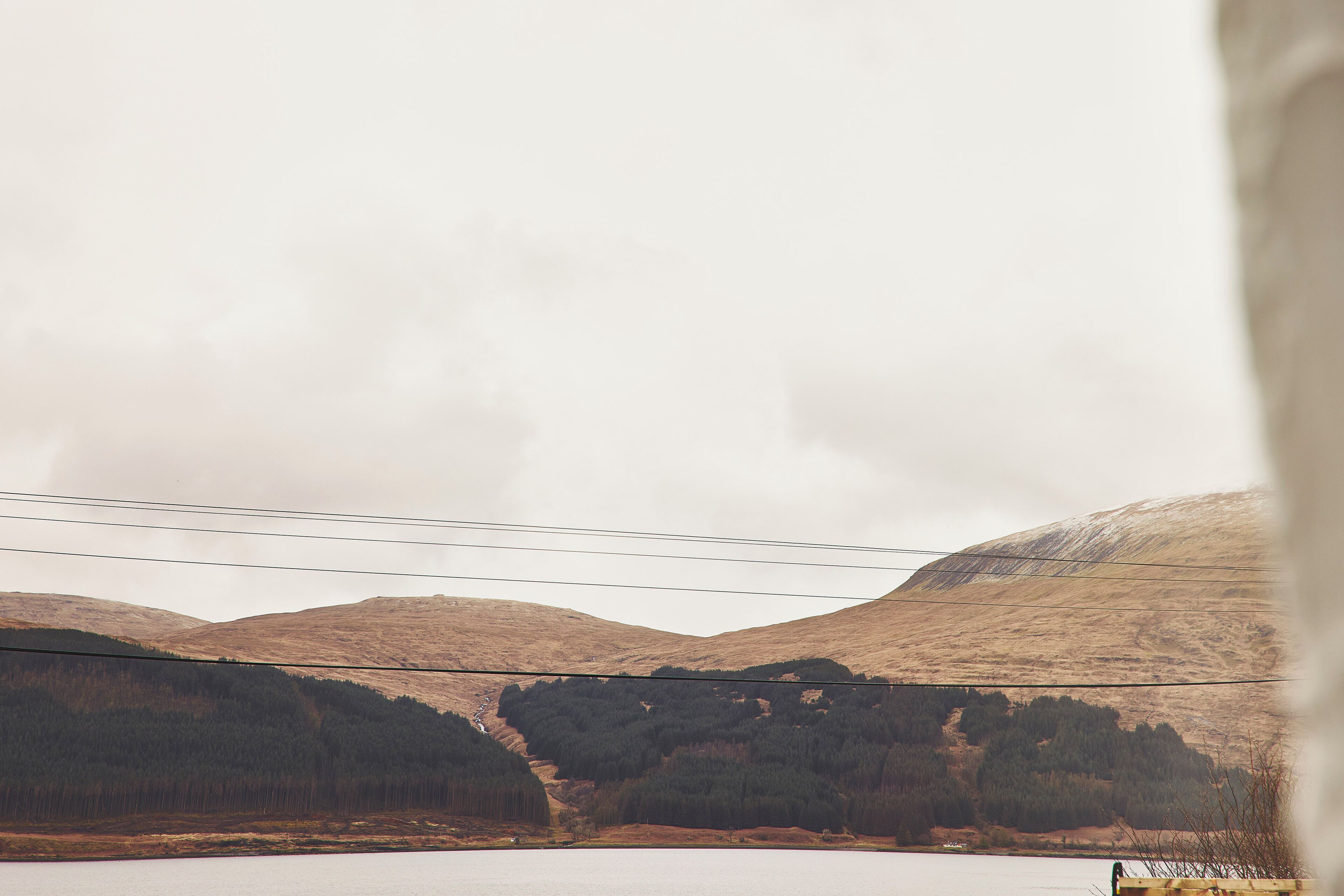 A mountainous landscape with a body of water, power lines, and a house in the distance.