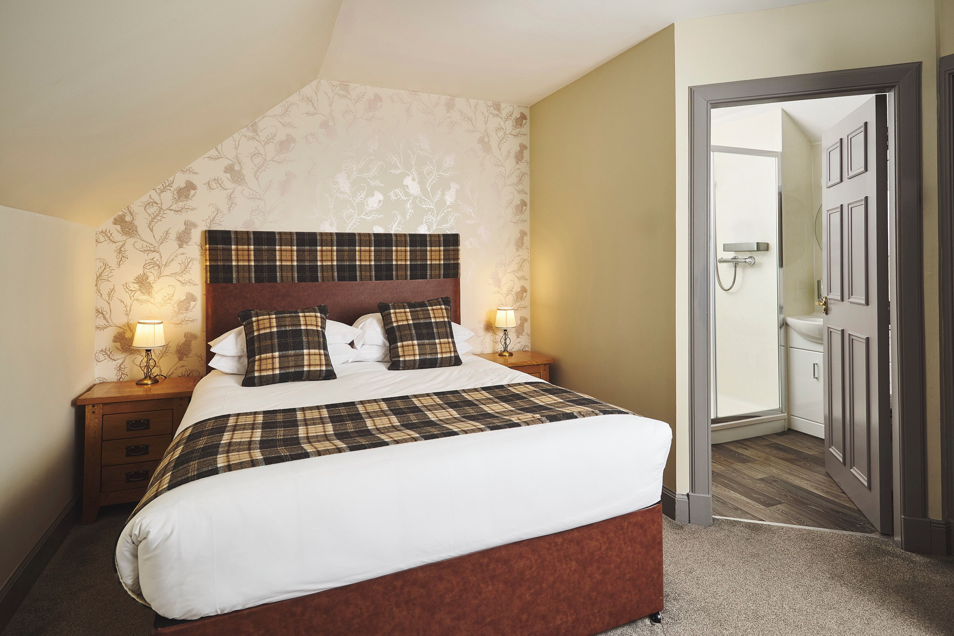 A bedroom with a bed, nightstands, a lamp, a door, and a view into another room.