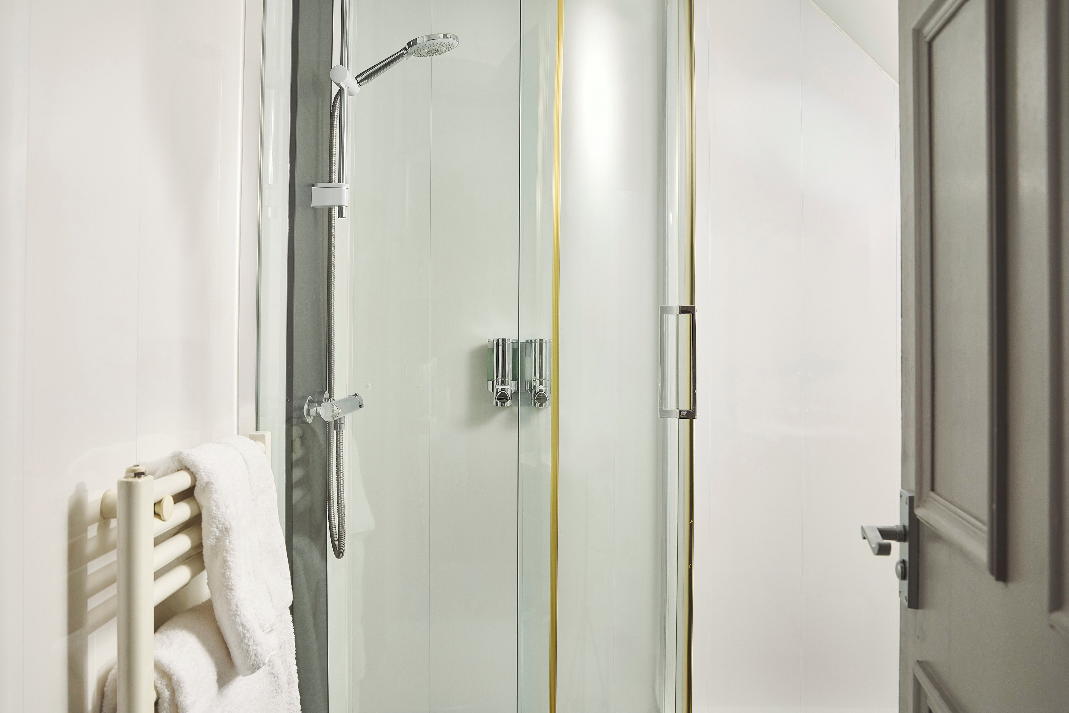 A modern bathroom with a glass-enclosed shower, a white towel rack, and a door with a golden stripe.