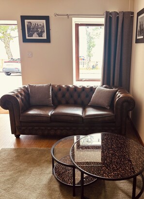 A brown leather sofa with a glass coffee table in front of a window with curtains. - Inn at Port nan Gael (Isle of Mull)