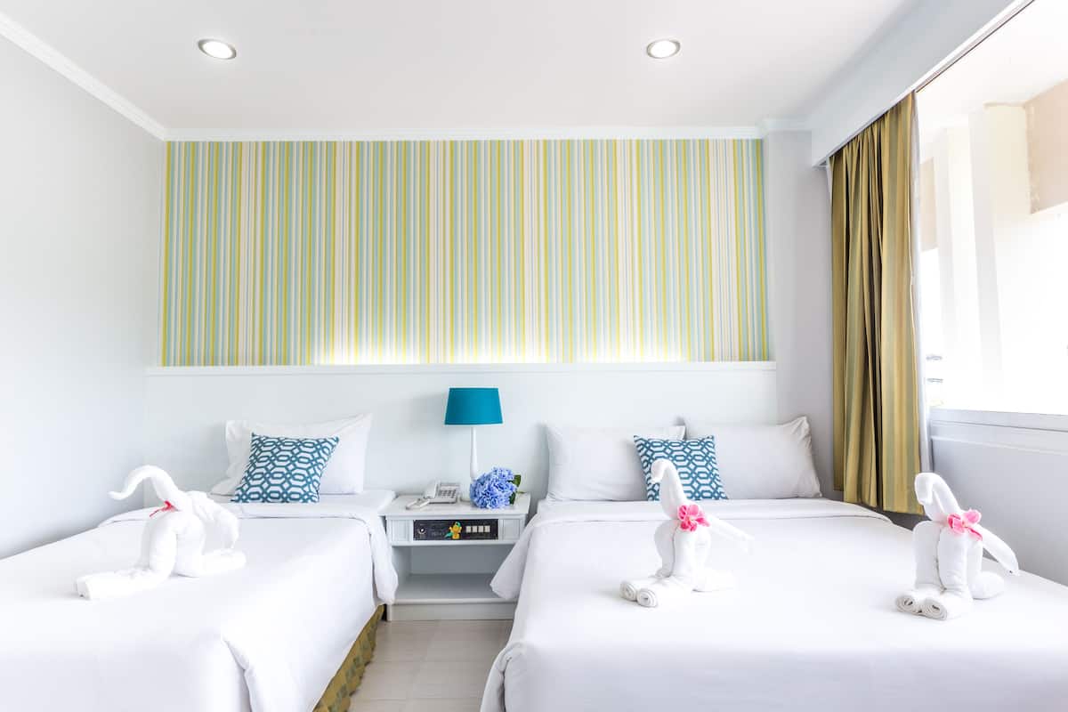 A hotel room with two beds, striped wallpaper, a blue lamp, and two swan-shaped towels.