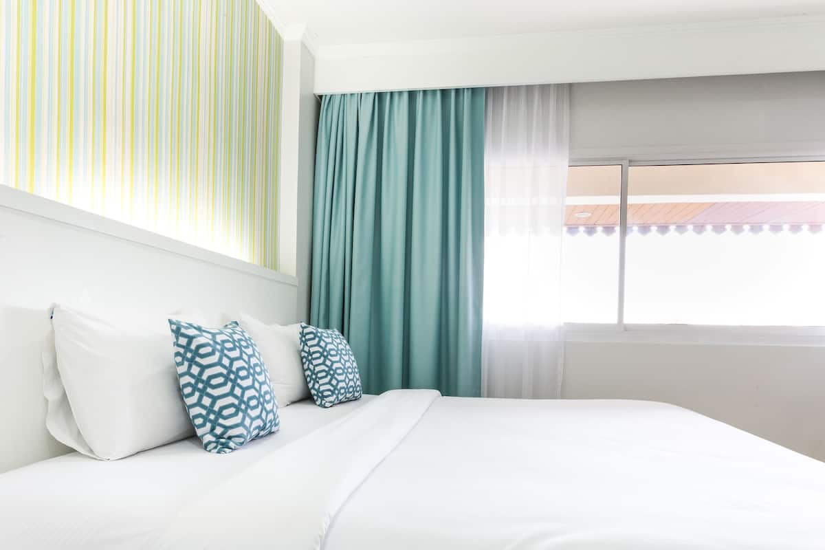 A hotel room with a bed, white bedding, and a window with curtains.