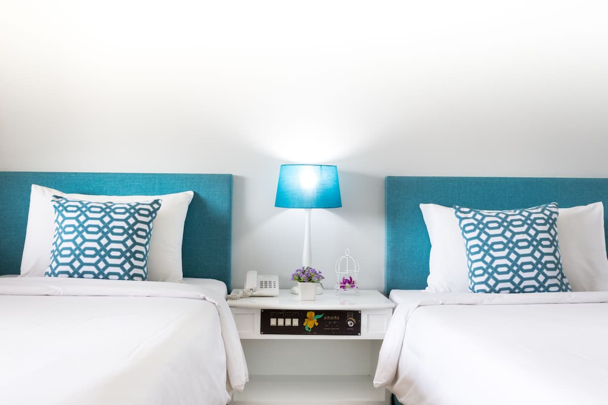A hotel room with two beds, each with a patterned pillow, a bedside table with a lamp, a phone, and a small vase with flowers.