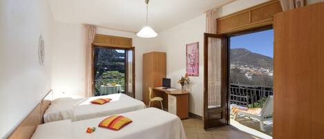Habitación de hotel con dos camas, un escritorio con computadora, una silla y un balcón con vistas a las montañas.