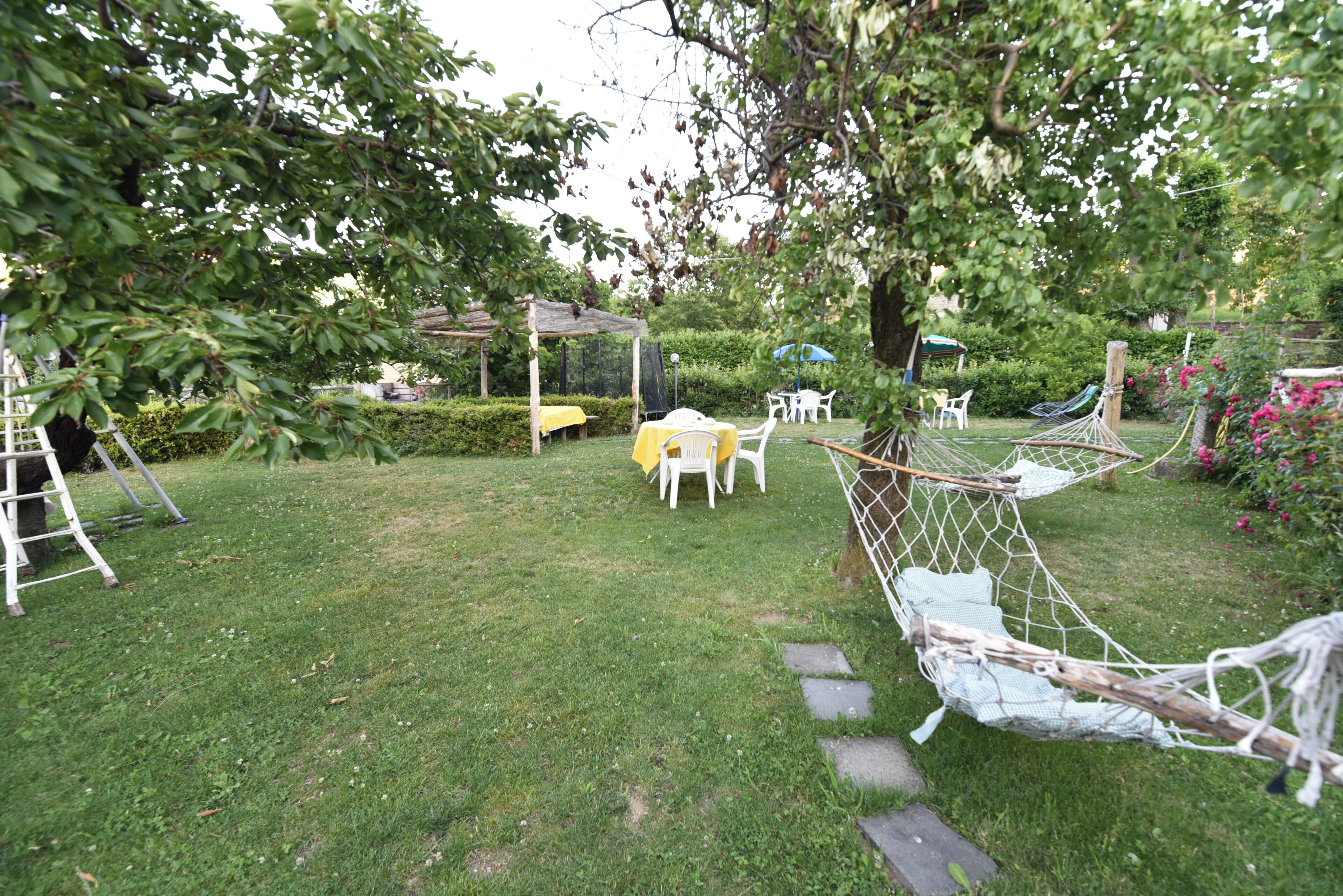 Un jardin avec un hamac, des chaises blanches et une table jaune.