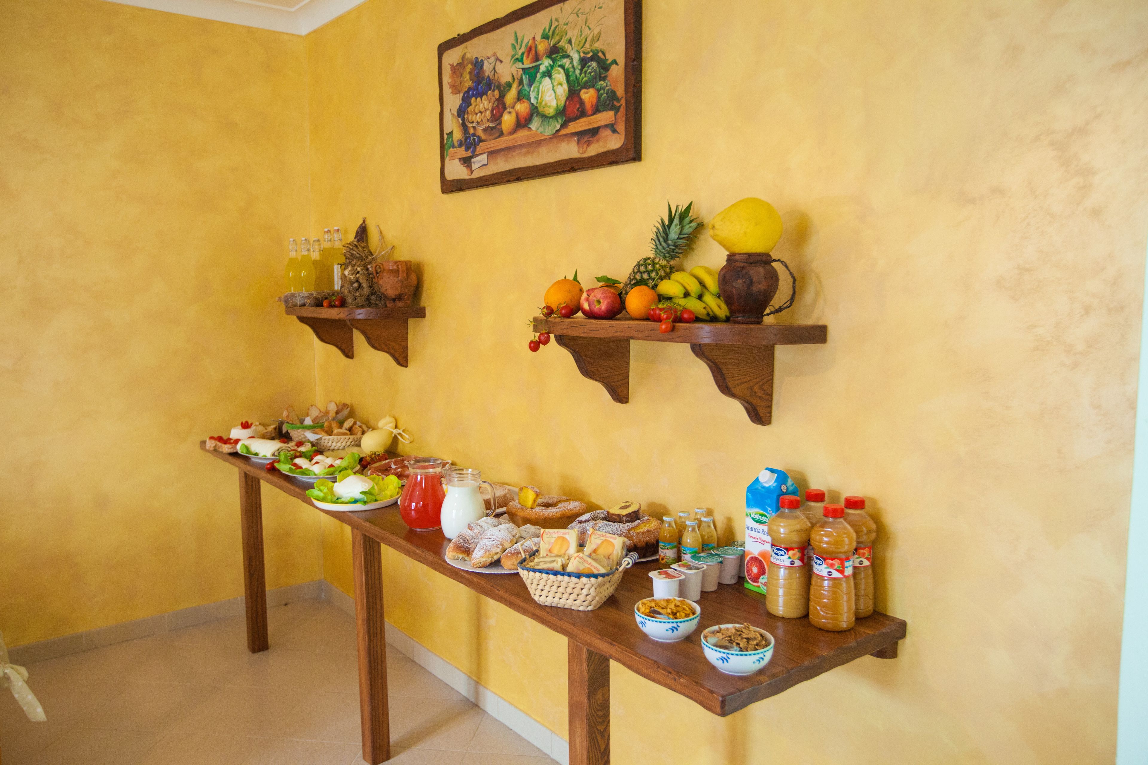 Ein Frühstücksbuffet mit verschiedenen Speisen und Getränken auf einem Holztisch vor einer gelben Wand.