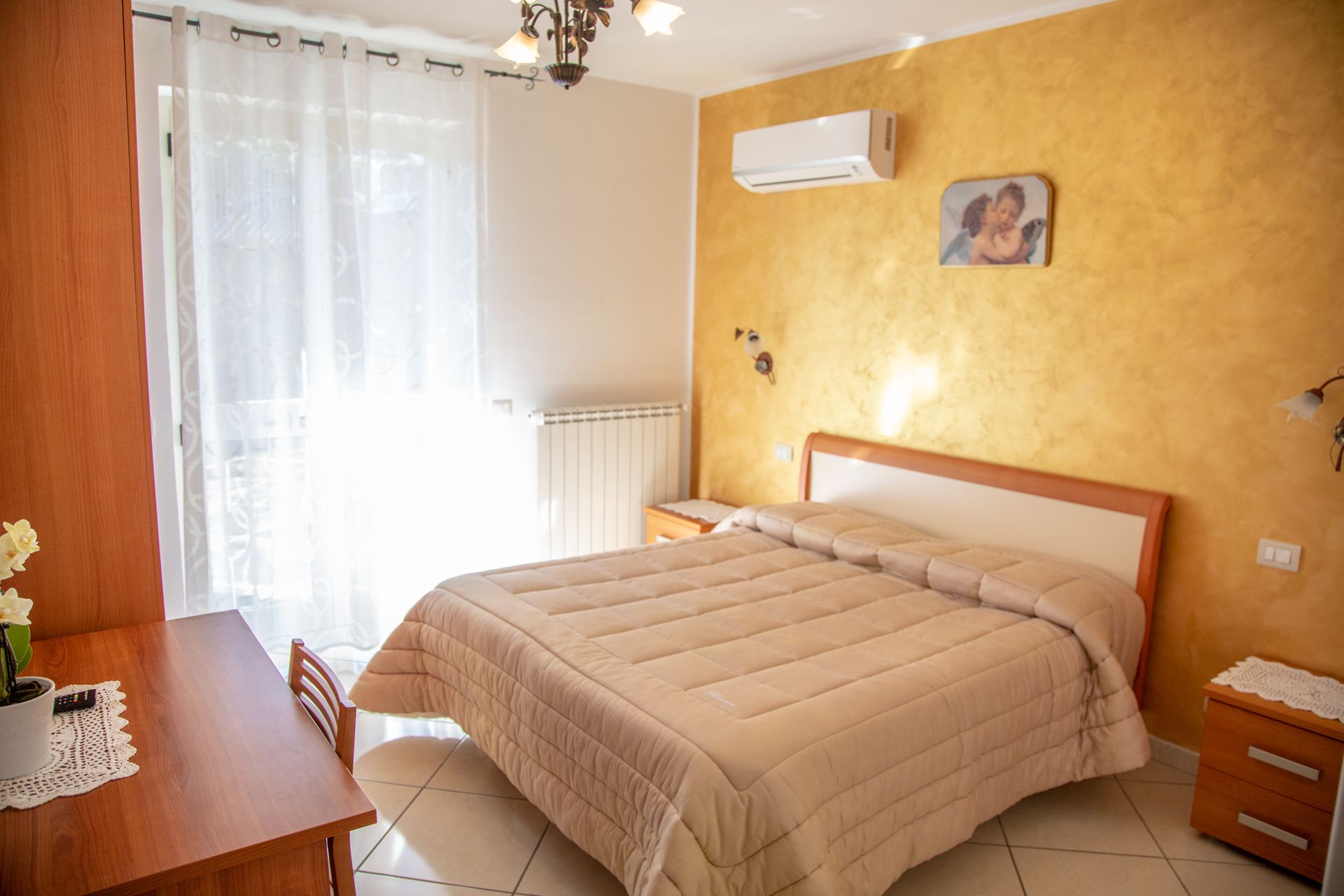 A bedroom with a bed, a wooden nightstand, a bedside table, and a wall-mounted air conditioner.