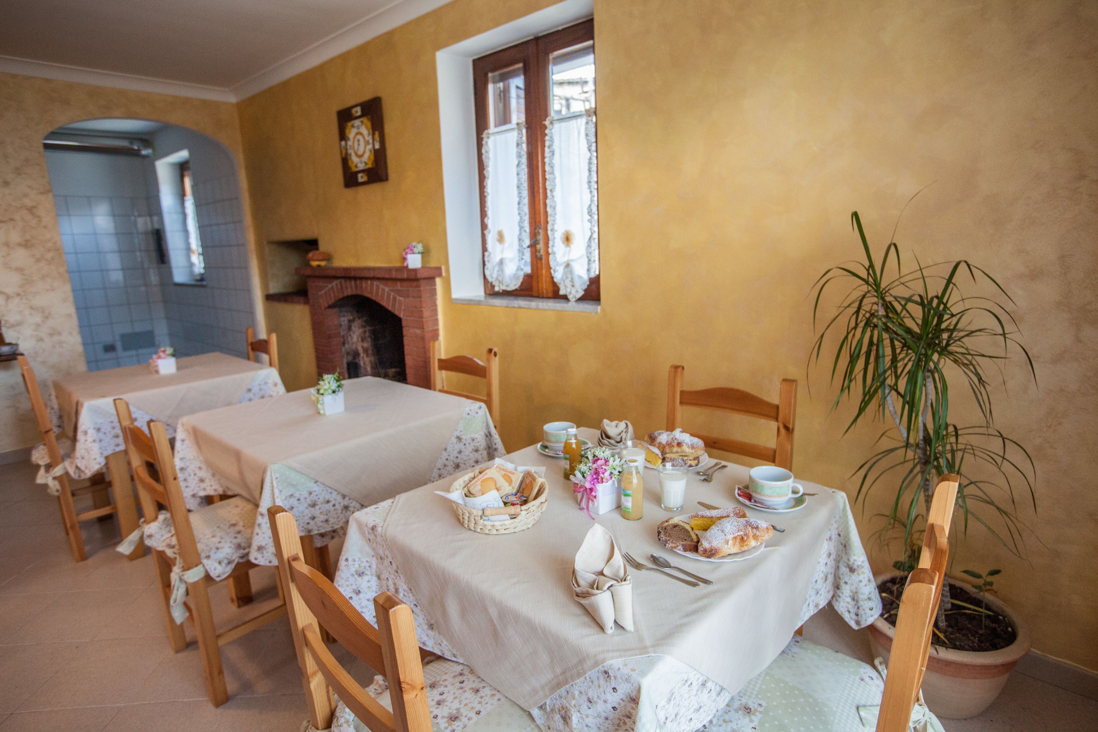 A dining area with tables set for breakfast, including bread, pastries, and beverages.