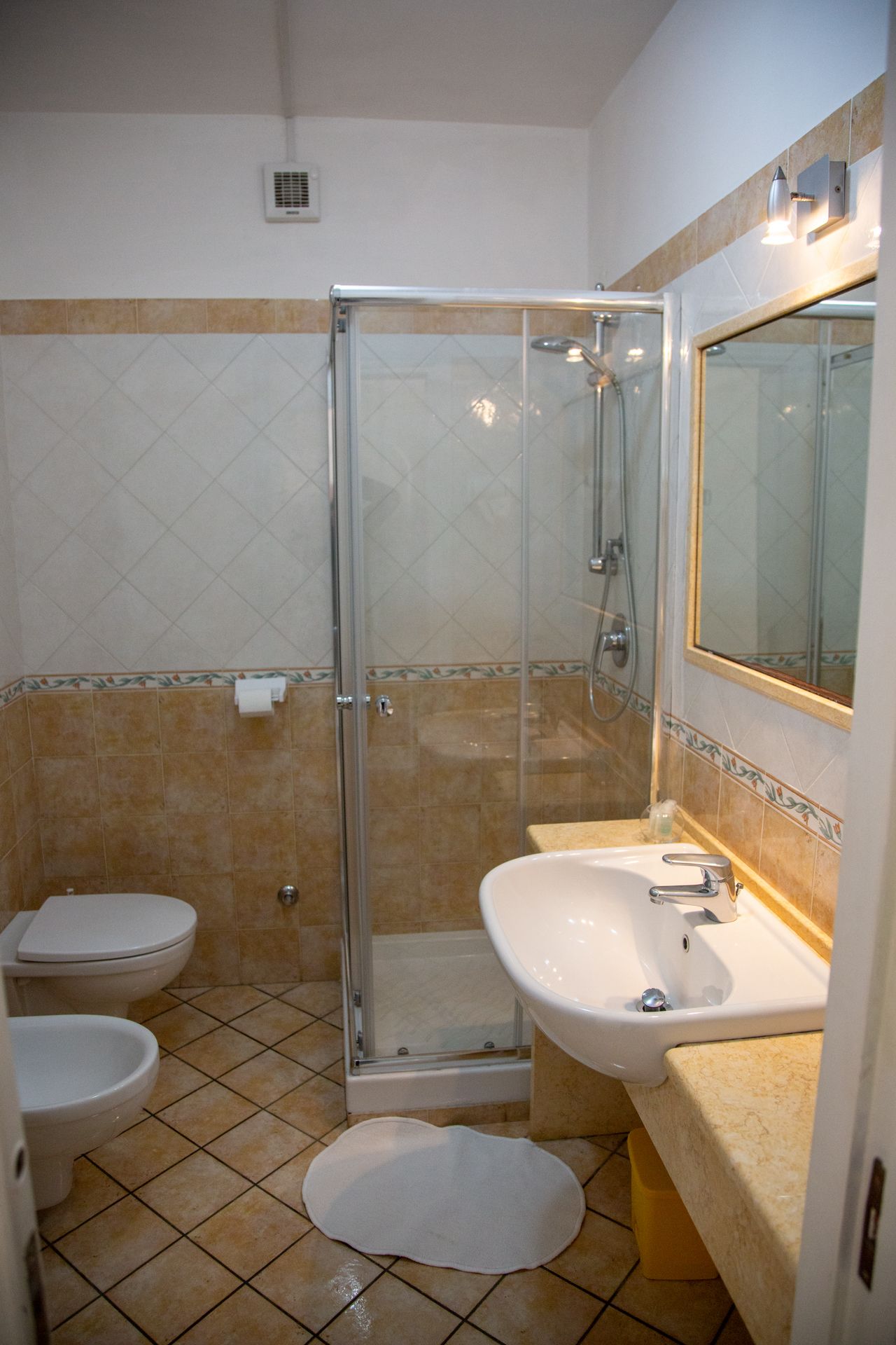 A bathroom with a glass-enclosed shower, two toilets, a sink, and a mirror.