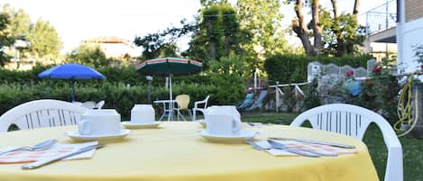 Un comedor al aire libre con mantel amarillo, sillas blancas y sombrilla azul.