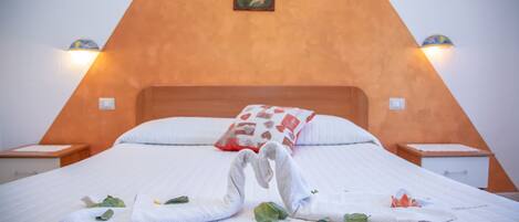 Una habitación triangular con una cama en el centro, un cuadro en la pared y dos lámparas de noche.
