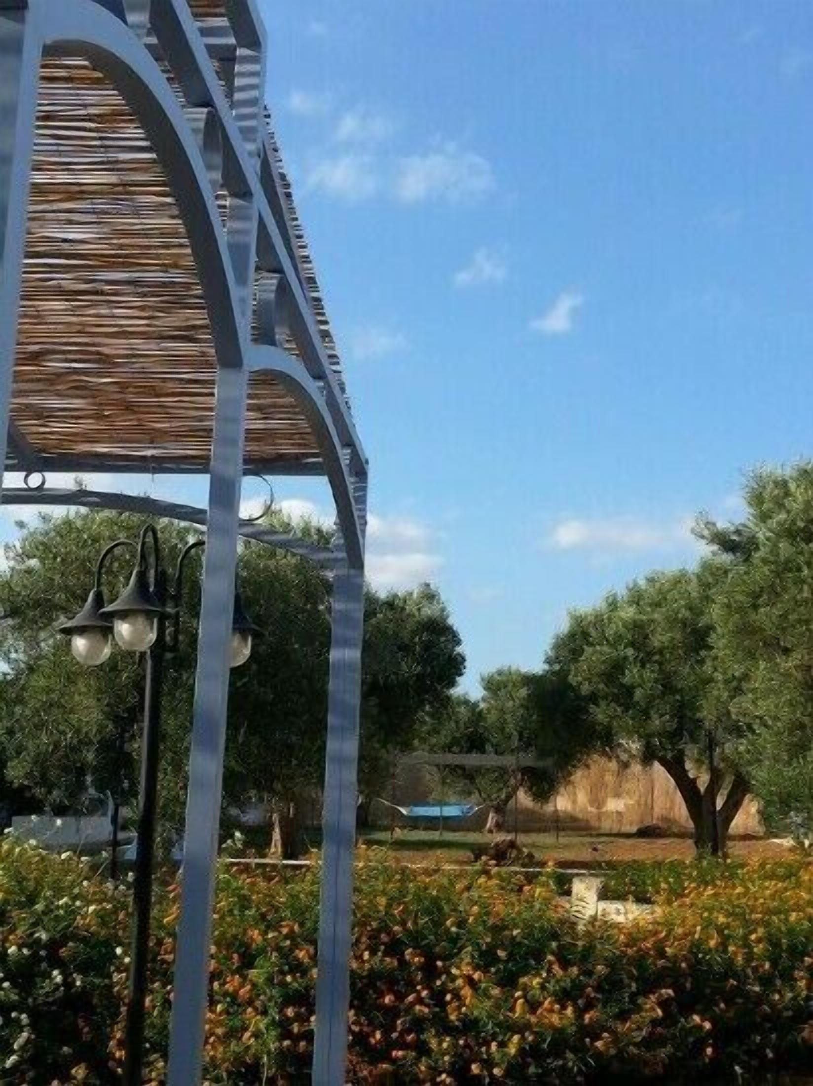 Un pabellón metálico con techo de madera, rodeado por un jardín con diversas plantas y flores.