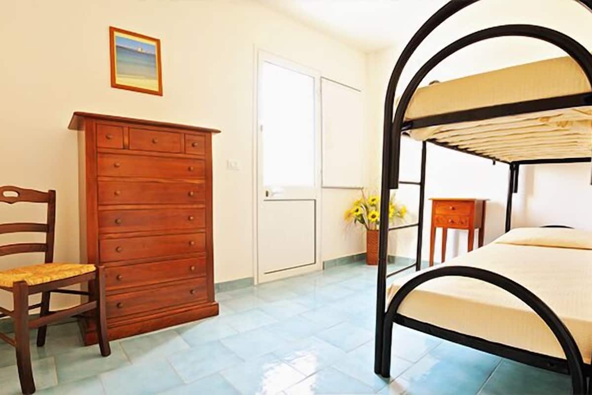 A bedroom with a bunk bed, a wooden dresser, a chair, and a door.
