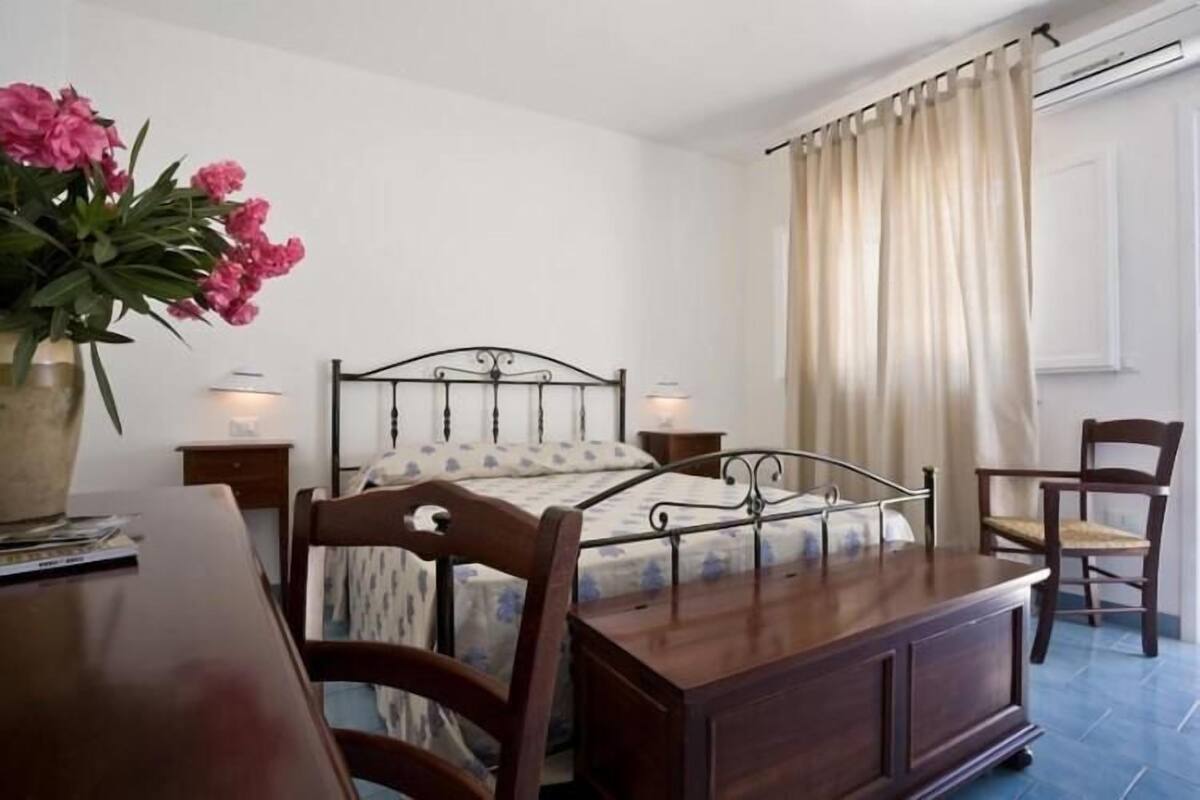 A bedroom with a bed, bedside tables, a chair, a wooden dresser, and a vase of flowers.