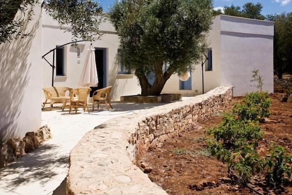 Un edificio blanco con un camino de piedra que lleva a una zona de estar con sillas y una mesa.