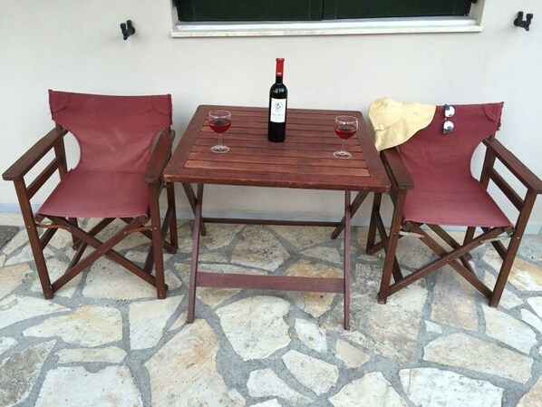 A wooden table with two chairs, a bottle of wine, and two glasses on a stone floor.