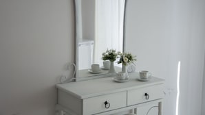 Une commode blanche avec un miroir au-dessus, un petit vase avec des fleurs et deux tasses sur lesquelles est inscrit le mot « HOME ».
