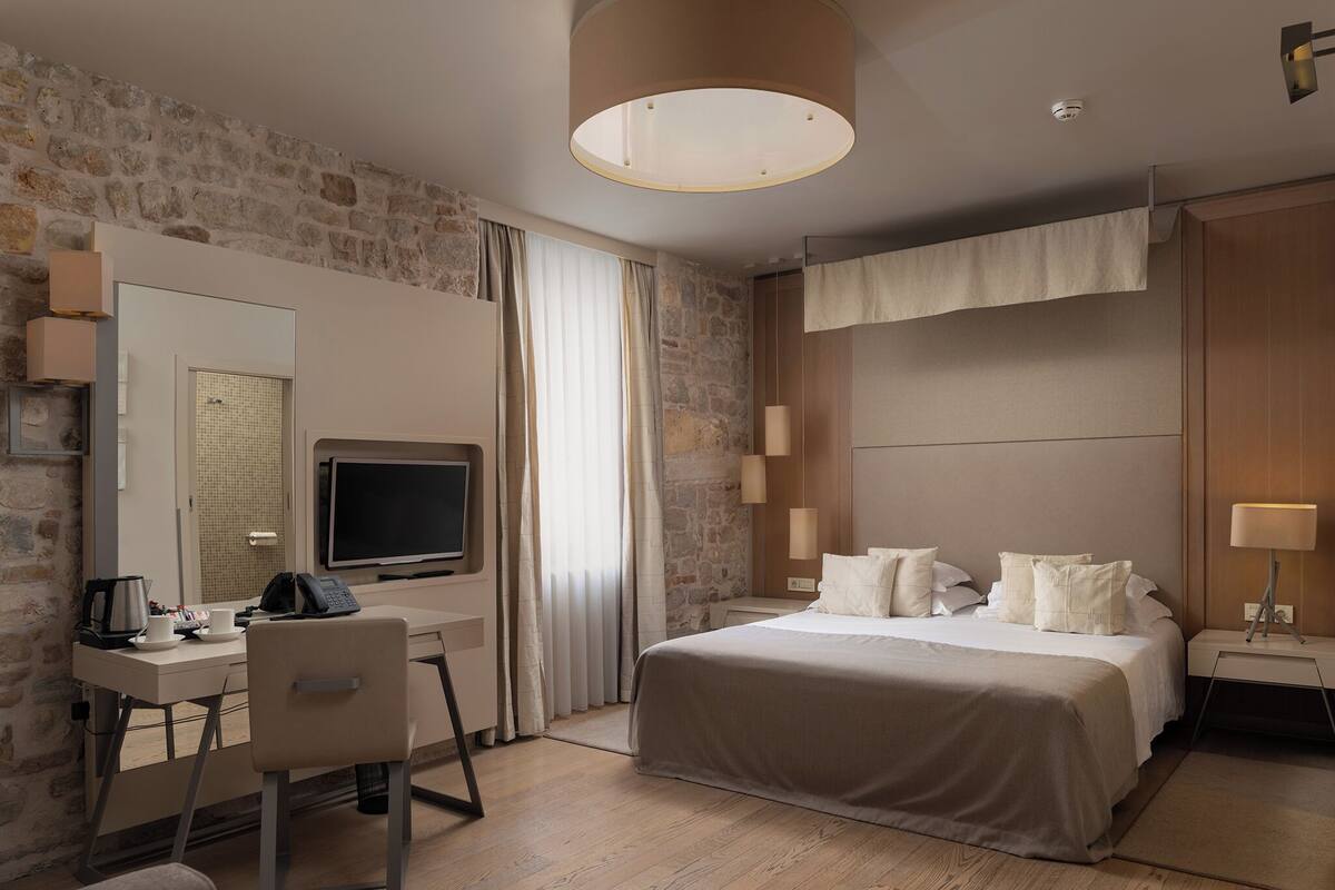 Ett hotellrum med en säng, ett skrivbord med en dator, en stol, en tv och en lampa.