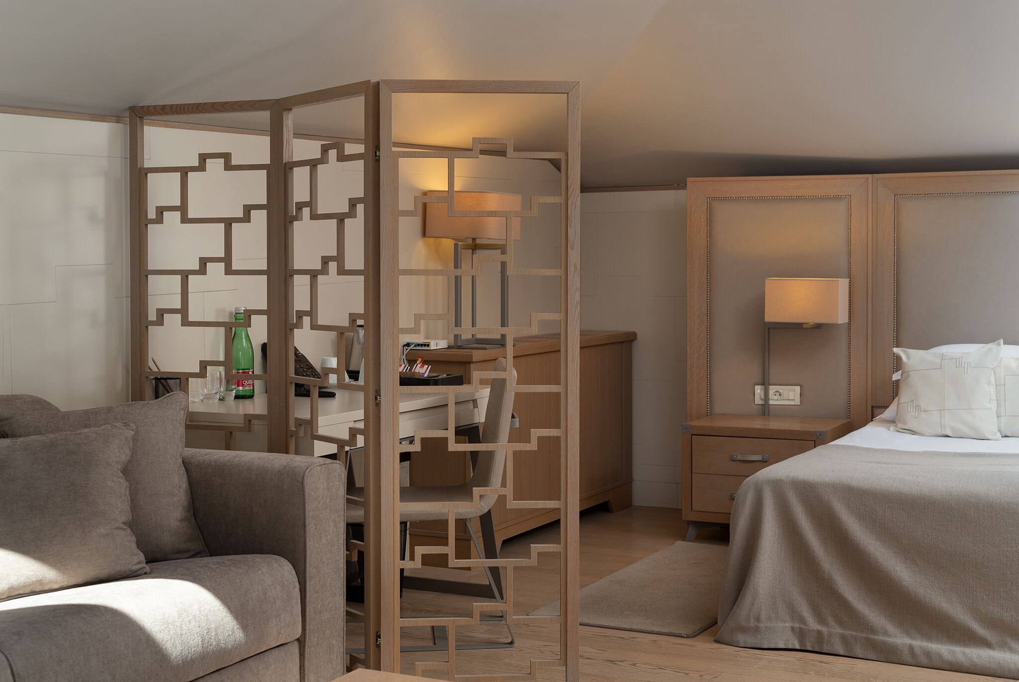 A hotel room with a wooden desk, a bed, a sofa, and a nightstand.