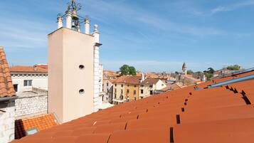 Blick auf terrakottafarbene Dächer und einen Turm mit einer Glockenkonstruktion.