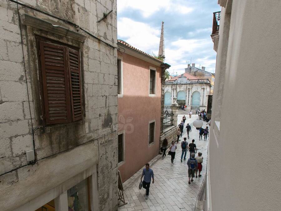 A narrow street with historic buildings, a tiled pavement, and pedestrians.