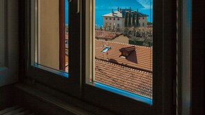 A window with a view of a building with a tiled roof and mountains in the background.