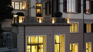 A multi-story hotel with illuminated windows and balconies, a flag, and a well-lit entrance.