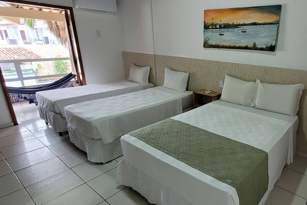 Habitación de hotel con dos camas individuales, una cama grande, un cuadro de un atardecer sobre el agua y una hamaca junto a la ventana.