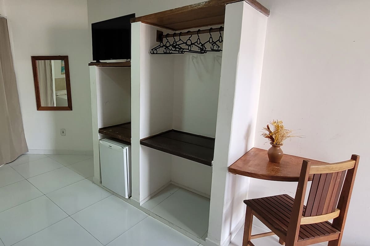 A compact room with a kitchenette, a small refrigerator, a wooden table with a chair, and a mirror on the wall.