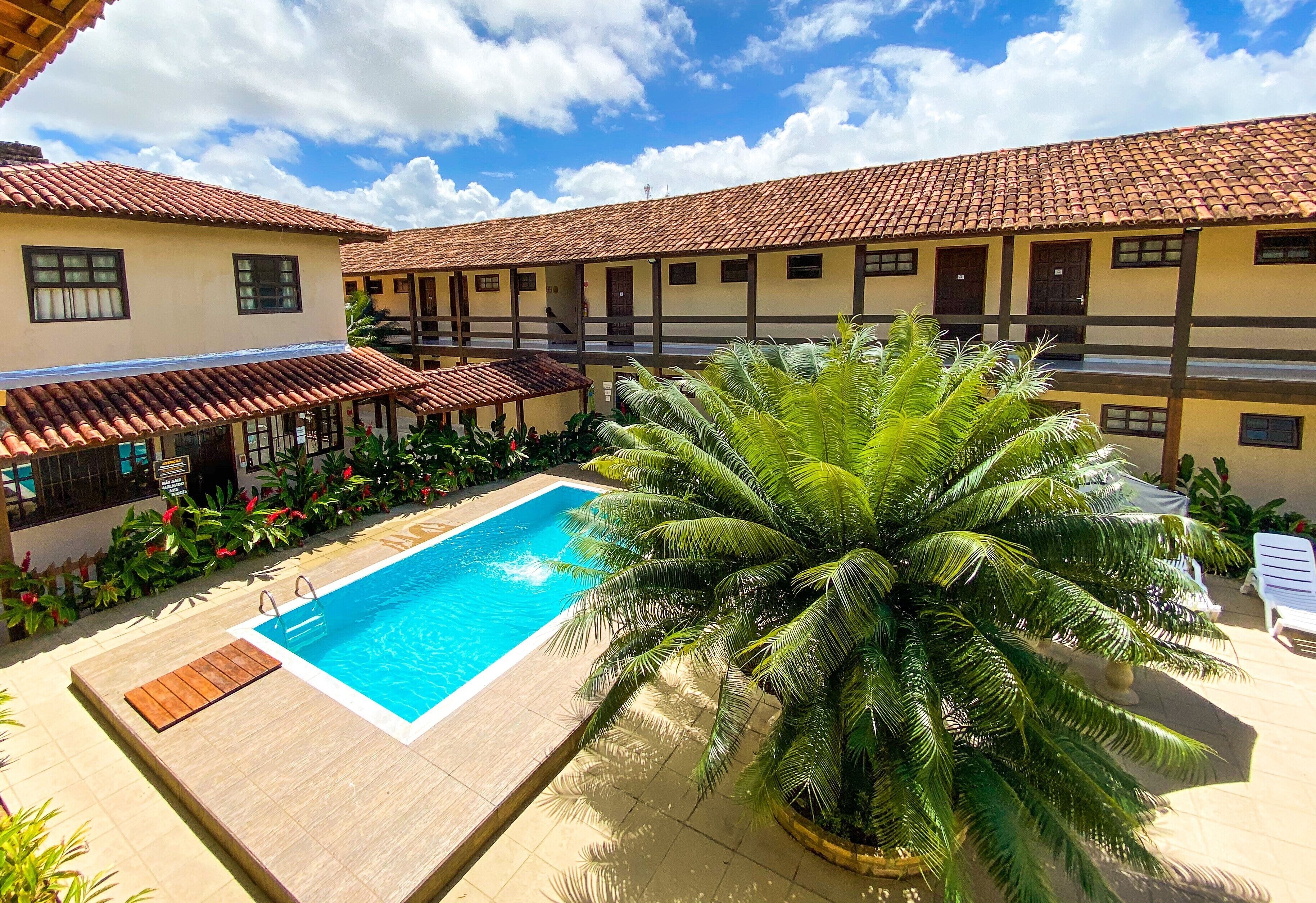 A swimming pool surrounded by a building with a tiled roof and a palm tree.