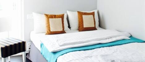 Una cama bien hecha con un almohadón a rayas, una mesita de noche y una lámpara de pared.