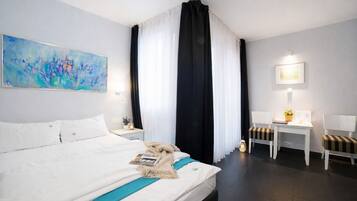 A hotel room with a large bed, a desk with two chairs, a small table with a plant, and a painting on the wall.