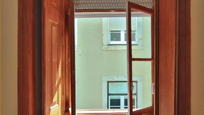 A room with a bed, a small table with a towel, and a window with wooden shutters.