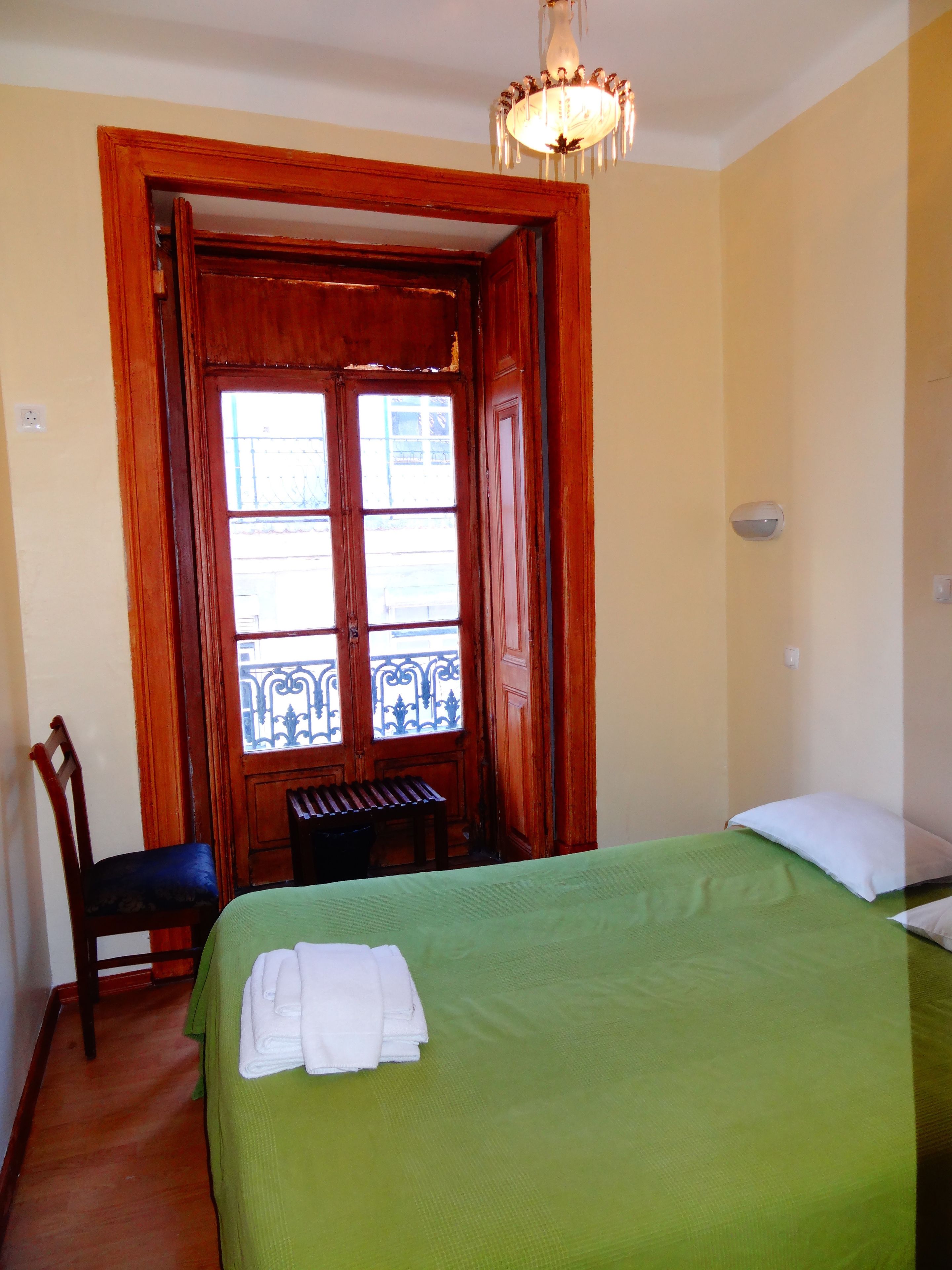 Una habitación con una cama, una silla, un banco y una puerta que da a un balcón exterior.