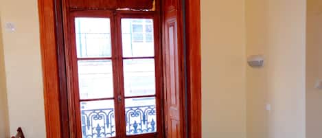 Una habitación con una cama, una silla, un banco y una puerta que da a un balcón exterior.