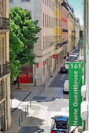 Vista da rua com edifícios, uma árvore e uma placa verde com 'Norte Guesthouse 161'.