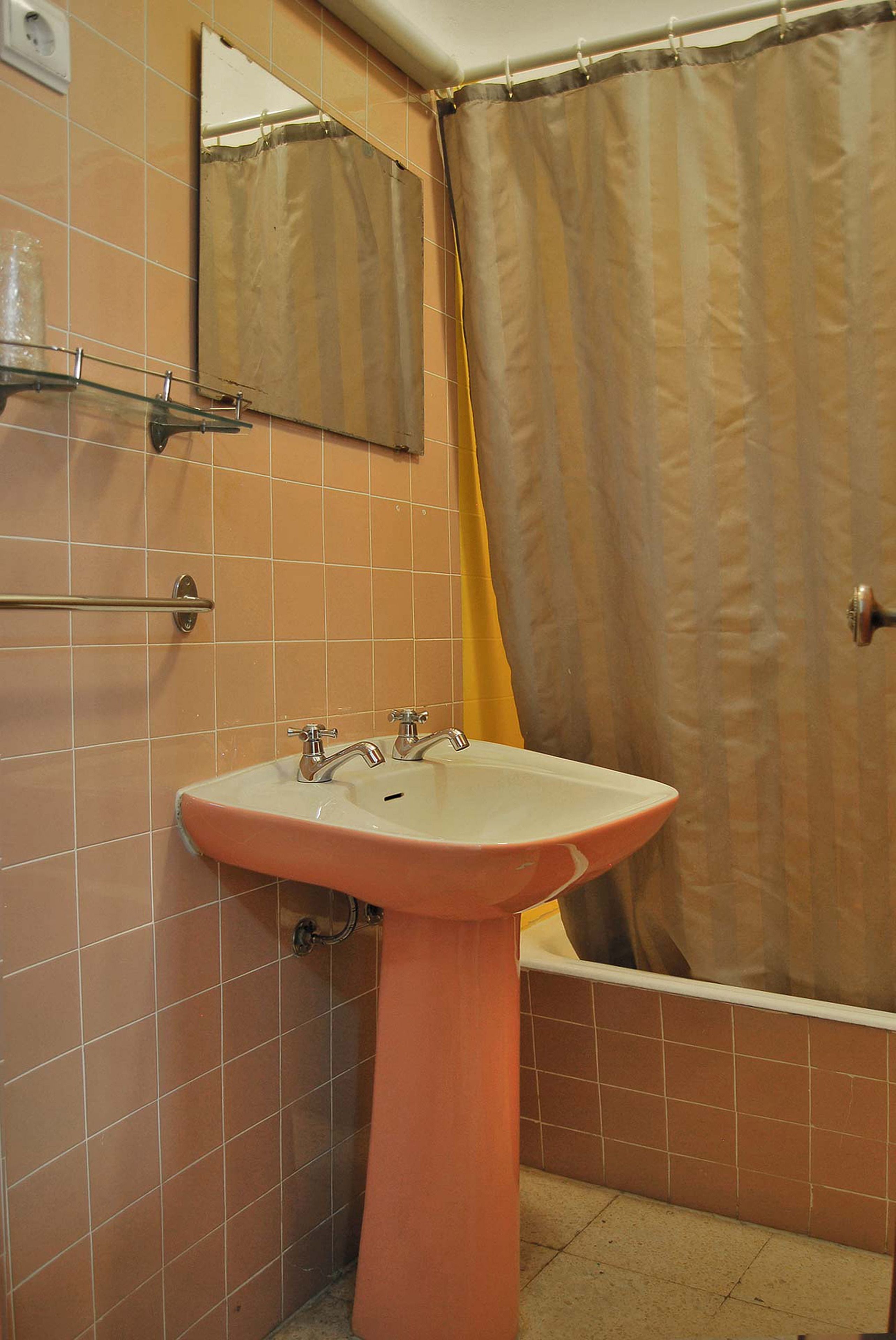 A bathroom with a pink sink, a mirror, and a shower curtain.