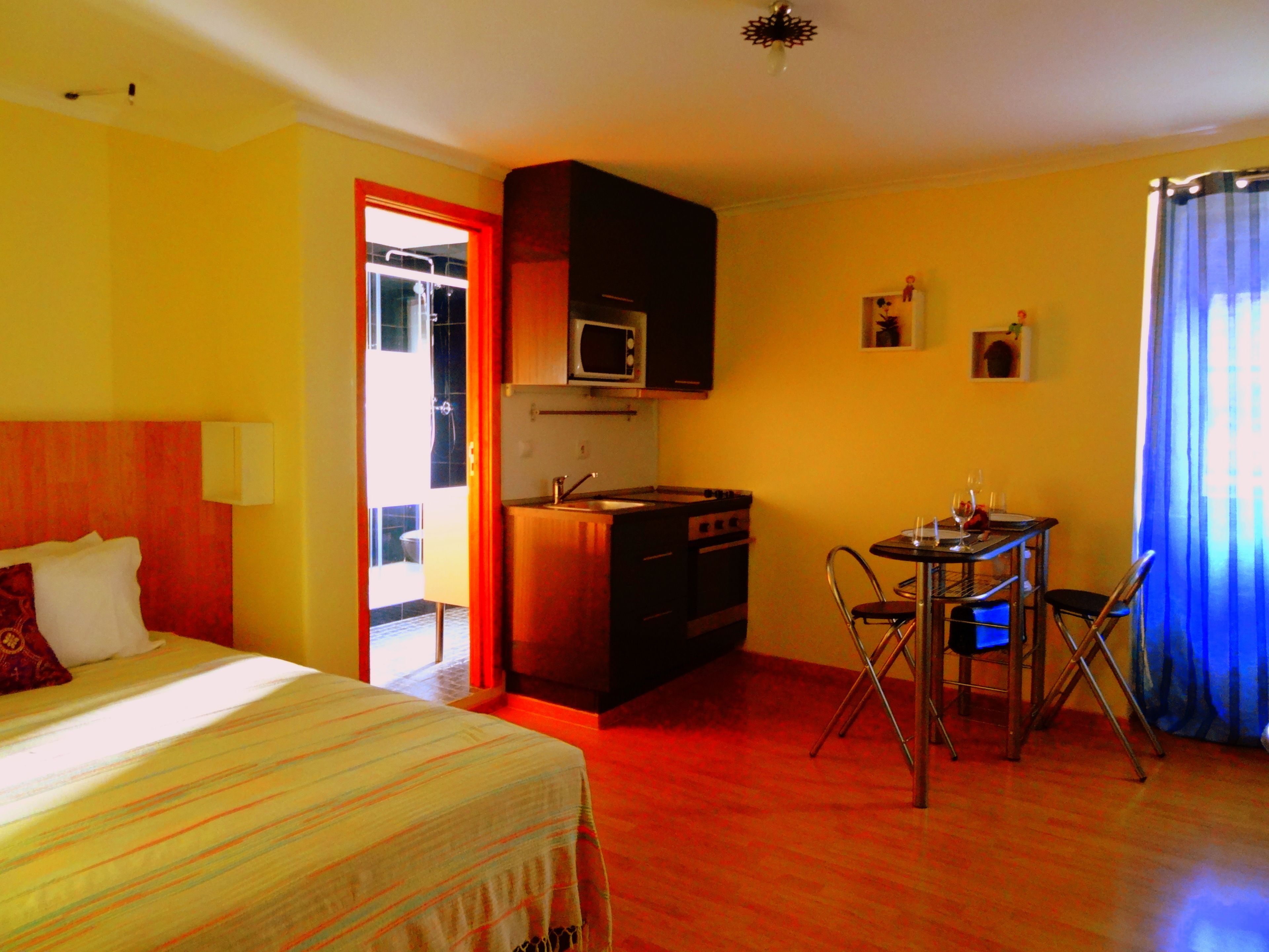A hotel room with a bed, a kitchenette, a dining area, and a bathroom.